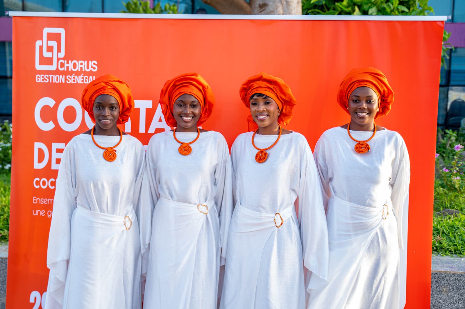 Hôtesses en tenue blanche et foulard orange devant le mur Chorus Gestion Sénégal