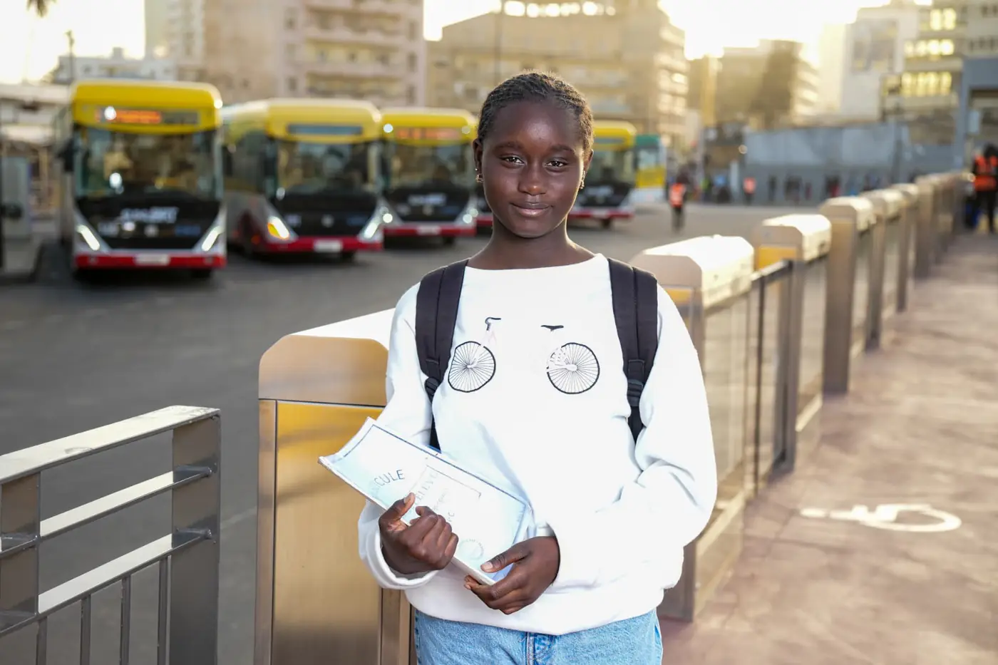 Jeune élève avec cahiers devant des bus, photographiée par KARIMKO pour le CETUD.
