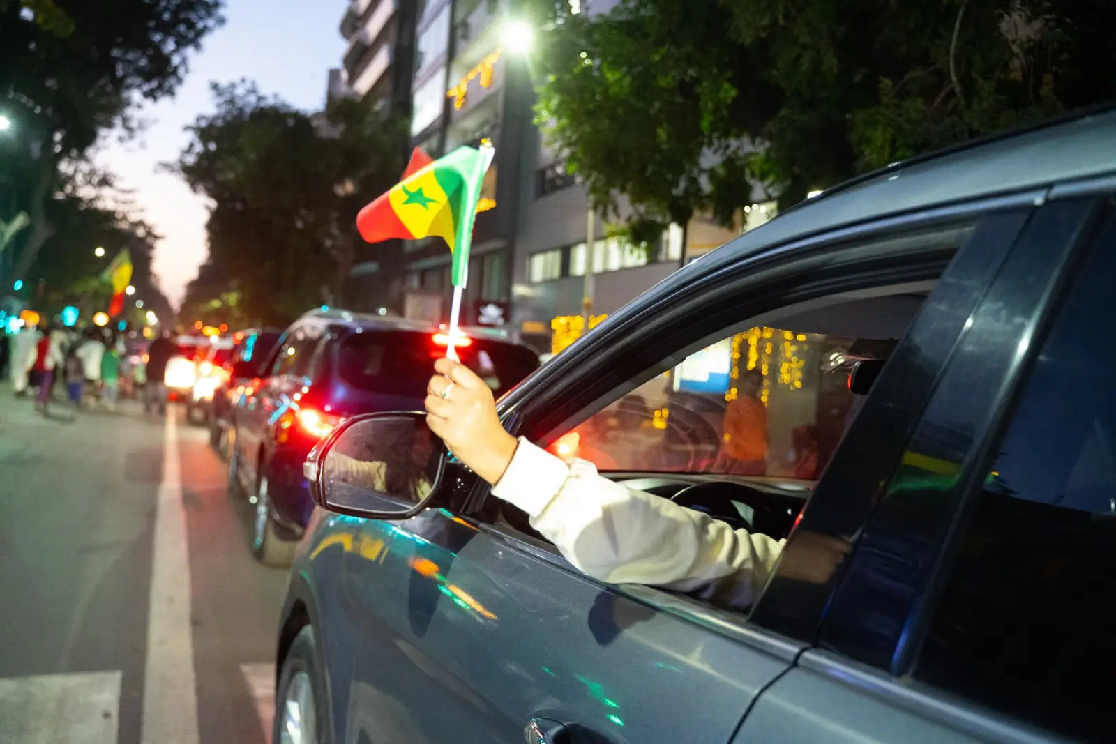 Main brandissant un drapeau du Sénégal depuis une voiture, de nuit à Dakar