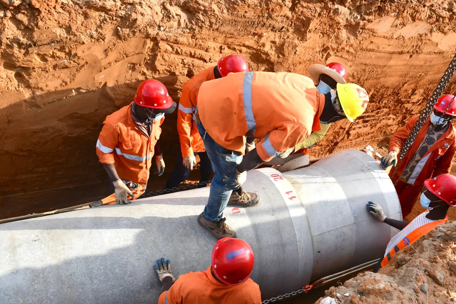 Ouvriers guidant une buse en béton au fond d'une tranchée