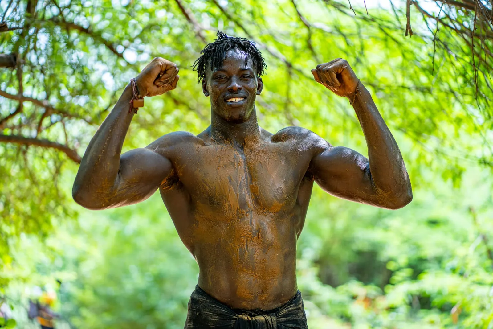 Lutteur souriant, bras levés sous les arbres
